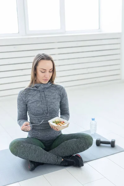 Deporte, estilo de vida saludable, concepto de la gente - Mujer rubia joven en ropa de fitness, con ensalada vegetariana saludable, sentado en el suelo — Foto de Stock