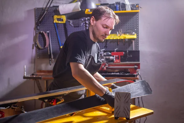 Un uomo in abiti da lavoro riparatore in officina servizio sci riparazione dello sci — Foto Stock