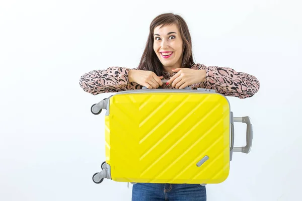 Mujer joven de pie con una maleta amarilla sobre el fondo de una pared blanca con espacio para copiar. El concepto de nuevos descubrimientos y la disponibilidad de viajes . — Foto de Stock