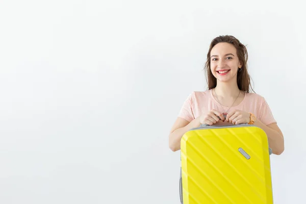 Портрет красивої молодої брюнетки з жовтою валізою в руках позує на білому тлі з копіювальним простором. Концепція подорожей та туризму . — стокове фото