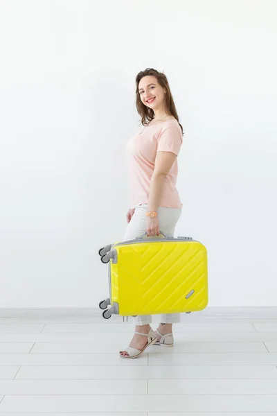 Joyful smiling young brunette woman posing with a yellow suitcase while waiting for a vacation. The concept of tourism and travel — Stock Photo, Image