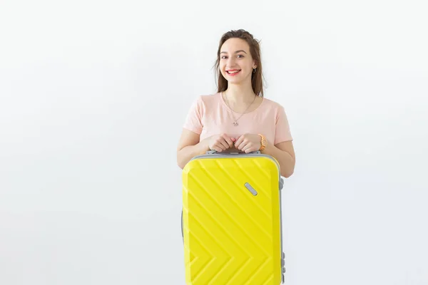 Vrolijke glimlachende jonge brunette vrouw poseren met een gele koffer tijdens het wachten op een vakantie. Het concept van toerisme en reizen — Stockfoto