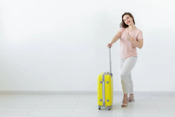 Retrato de una hermosa joven morena con una maleta amarilla en las manos posando sobre un fondo blanco con espacio para copiar. Concepto de viajes y turismo . — Foto de Stock