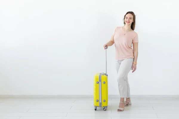 Porträt einer schönen jungen brünetten Frau mit einem gelben Koffer in der Hand, die vor weißem Hintergrund mit Kopierraum posiert. Reise- und Tourismuskonzept. — Stockfoto