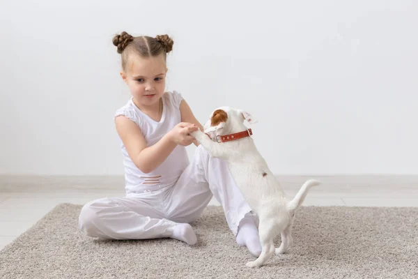 Concepto de personas, niños y mascotas - niña pequeña sentada en el suelo con un lindo cachorro Jack Russell Terrier — Foto de Stock