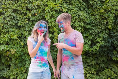 Tatil, bayram ve insanlar kavramı - mutlu çift yüzlerinde çok renkli toz ile eğleniyor