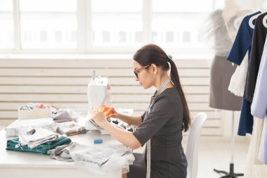İnsanlar, terzi ve moda kavramı - yan görünüm portre moda tasarımcısı bardaklarda atölyede dikiş makinesi kullanma