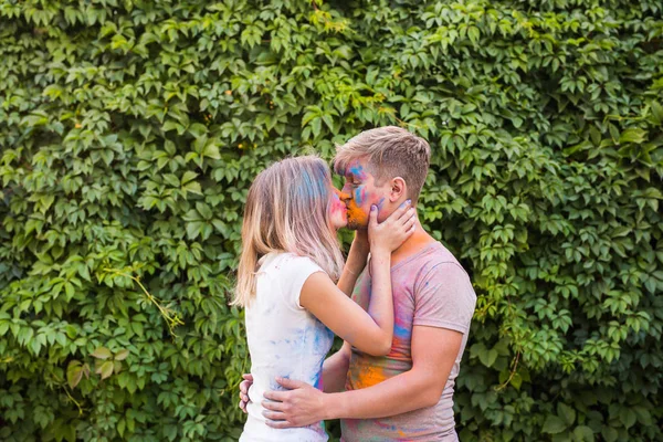 Concepto de vacaciones, vacaciones y personas - Pareja feliz divirtiéndose y besándose con polvo multicolor en sus caras — Foto de Stock