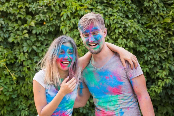 Conceito de férias, holi e pessoas - Casal feliz se divertindo com pó multicolorido em seus rostos — Fotografia de Stock