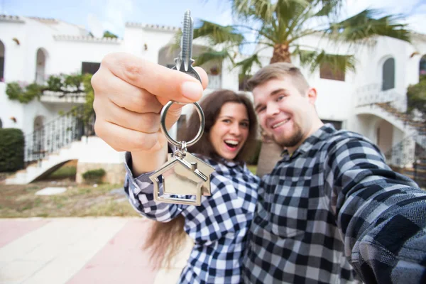 Propiedad, bienes raíces y concepto de apartamento - Feliz pareja joven y divertida mostrando las llaves de su nueva casa —  Fotos de Stock