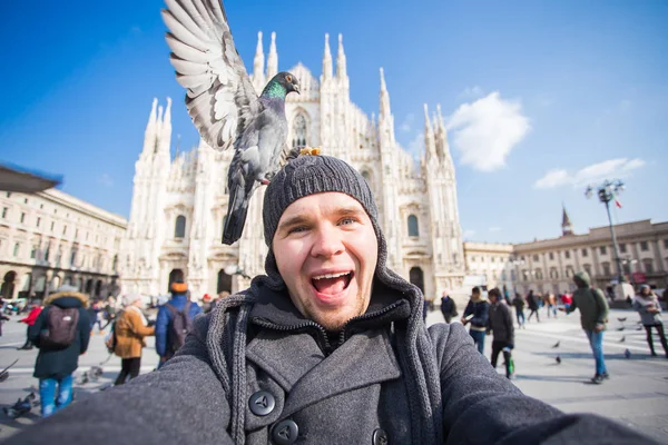 Winter travel, vacations and birds concept - Young funny man taking selfie with pigeons near Milan Cathedral Duomo di Milano, Italy.