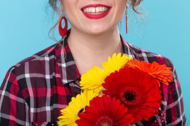Mavi bir arka plan aleyhine poz elinde parlak gerbera çiçek bir buket tutan ekose gömlek tanımlanamayan gülümseyen güzel genç kadın. Tatil ve hediyeler kavramı.
