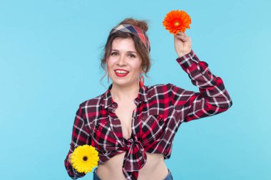 Elinde mavi bir arka plan üzerinde poz iki kırmızı ve turuncu çiçek tutan Büyüleyici genç gülümseyen kadın. Güzellik ve öz bakım kavramı.