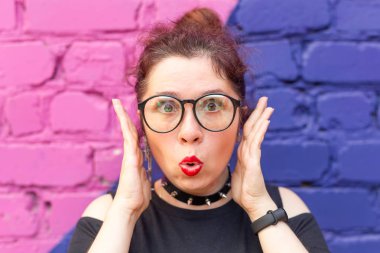 Mavi-mor tuğla arka plan üzerinde poz şık giysiler ve gözlük deli bir genç pozitif öğrenci kız Portresi