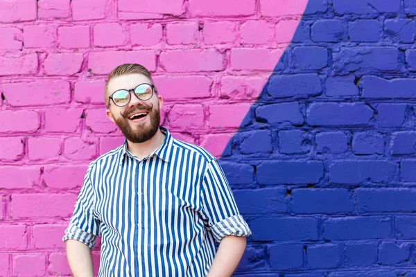 Retrato é um cara estudante jovem agradável com um bigode e uma barba posando contra uma parede de tijolo azul-violeta com espaço de cópia . — Fotografia de Stock