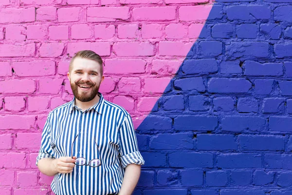 Retrato é um cara estudante jovem agradável com um bigode e uma barba posando contra uma parede de tijolo azul-violeta com espaço de cópia . — Fotografia de Stock