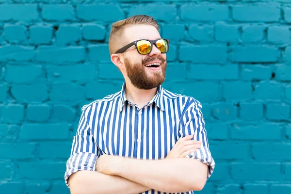 Portré vidám pozitív stílusos tanuló srác a szemüveg egy bajuszos és szakállát jelentő kék fal ellen. A sikeres vidám emberek koncepciója. — Stock Fotó