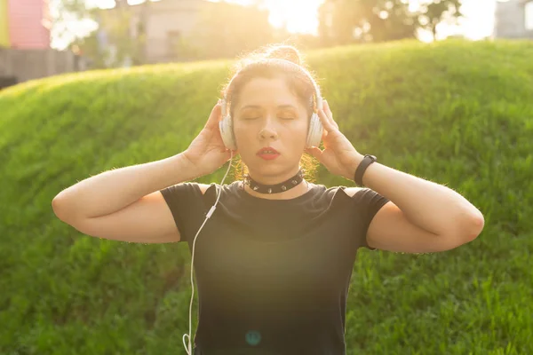 Beautiful sensual young woman listens to music with headphones while walking through the park on a sunny evening. Weekend getaway concept.