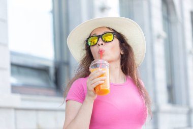 Sıcak bir yaz gününde şehirde dolaşan şapka ve gözlüklü güzel ve şık genç bir kadının yakın çekim portresi. Mutlu pozitif insanlar kavramı.