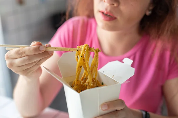 Blízkou rukou mladé neidentifikované dívky pojídáním čínských nudlí s dřevěnými hůlky, které sedí v kavárně. Koncepce asijských kuchyní. — Stock fotografie