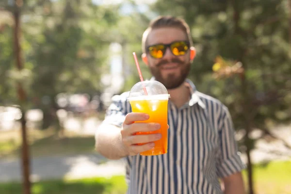 Portret van een positieve vrolijke jongeman met een glas sap met een rietje tijdens het wandelen in het Park op een warme zonnige zomerdag. Het concept van rust na studie en werk in het weekend. — Stockfoto