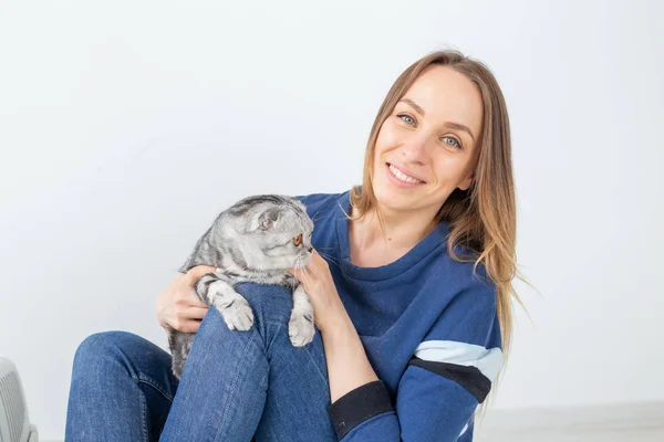 Charmante jeune femme positive tient dans ses mains son beau chat écossais pli gris assis sur le sol dans un nouvel appartement. Concept animal de compagnie . — Photo
