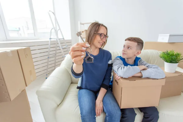Размытые позитивные мама и сын сидят на диване и показывают ключи от новой квартиры. Концепция покупки жилья в кредит и новоселье . — стоковое фото