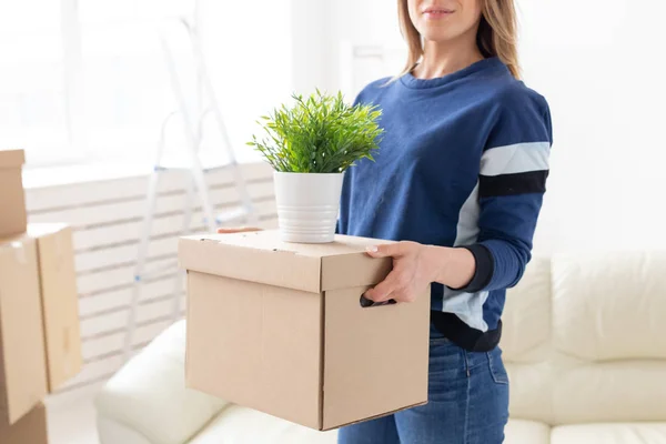 Jovem não identificada tem uma caixa e um pote de plantas enquanto se muda para um novo apartamento. Acolhimento e novo conceito de habitação . — Fotografia de Stock