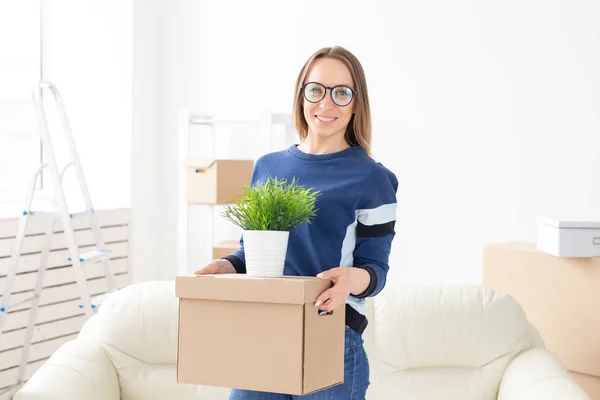 Jovem tem uma caixa e um pote de plantas enquanto se muda para um novo apartamento. Acolhimento e novo conceito de habitação . — Fotografia de Stock