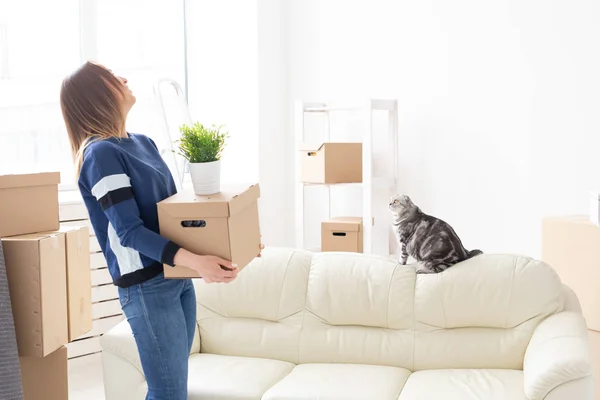 Очаровательная молодая женщина держит коробку с вещами во время переезда, стоя в новой квартире рядом со своим седоухим шотландским котом. Концепция переезда и новоселья . — стоковое фото
