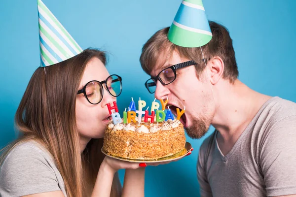 Zbliżenie z Bizarre młody para dziewczyna i chłopak w papier kapelusze chcieć do bite od kawałek z gratulacyjny ciasto. Koncepcja urodzin i gratulacji. — Zdjęcie stockowe