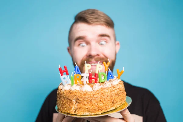 Louco engraçado cara positivo hipster segurando um bolo de aniversário feliz em suas mãos de pé sobre um fundo azul. Conceito de piadas e cumprimentos de férias . — Fotografia de Stock