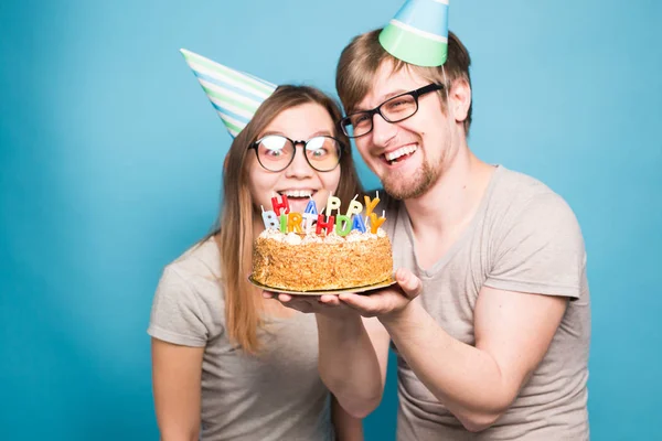 재미 괴상한 남자와 여자는 파란색 배경위에 촛불과 생일 케이크를 들고 휴일 모자와 안경을 착용 — 스톡 사진