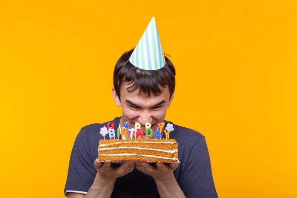 Divertido chico positivo en gafas sostiene en sus manos un pastel casero con la inscripción feliz cumpleaños posando sobre un fondo amarillo. Concepto de vacaciones y aniversarios . —  Fotos de Stock
