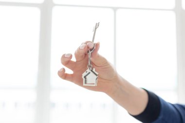 Mortgage konsepti. Ev şeklinde anahtarlık ile kadın el tutma anahtarı. Modern ışık iç. Gayrimenkul, eve taşınma veya mülk kiralama.