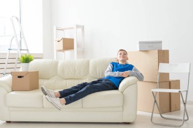 Tehcir, yeni ev ve çocuk kavramı - Memnun mutlu genç çocuk yeni daireye taşıma sırasında kanepeüzerinde yatıyor