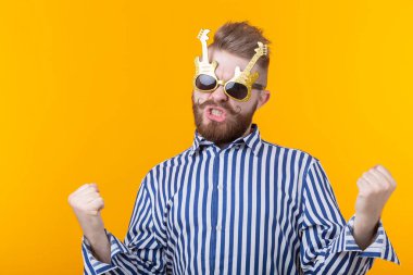 Gitar şeklinde gözlüklü pozitif genç adam sarı bir arka plan karşı sevinir. Kutlama ve partiler kavramı.