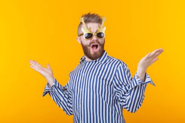 Gitar şeklinde gözlüklü pozitif genç adam sarı bir arka plan karşı ellerini kaldırdı sahip sevinir. Kutlama ve partiler kavramı.