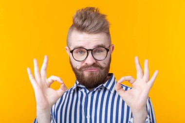Bıyıklı ve sakallı, gözlüklü yakışıklı genç adam sarı bir arka plan üzerinde poz veren ok gösterir. Şans ve berber kavramı.