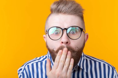 Bıyık ve sakallı genç adam sarı bir arka planda sürpriz gözleri şişkinleme yapıyor. Sürpriz ve belirsizlik kavramı.