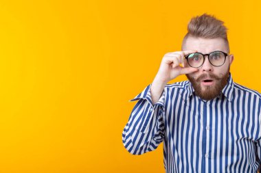 Bıyıklı ve sakallı genç hipster adam kopya alanı ile sarı bir arka plan üzerinde poz gözlük ile bakar. Sürpriz kavramı.