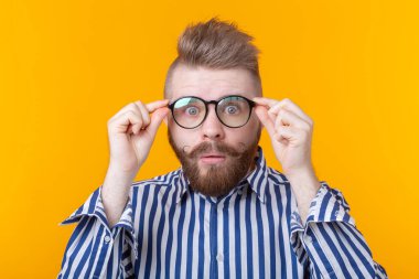 Bıyıklı ve sakallı genç hipster adam sarı bir arka plan üzerinde poz gözlük ile bakar. Sürpriz kavramı.