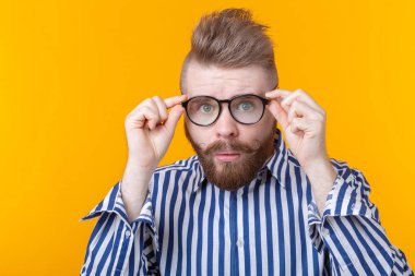 Bıyıklı ve sakallı genç hipster adam sarı bir arka plan üzerinde poz gözlük ile bakar. Sürpriz kavramı.