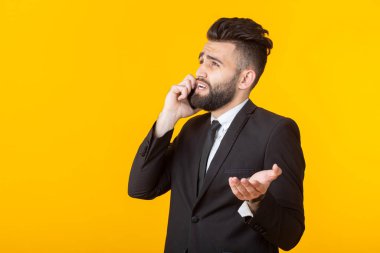 Resmi kıyafetler içinde sakallı sevimli genç adam sarı bir arka plan üzerinde poz telefonda konuşurken. Gayri resmi toplantı ve iş anlaşması kavramı.