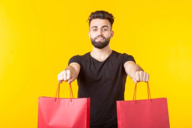 Adam sarı bir arka planda kırmızı alışveriş torbaları tutuyor. Süpermarket ve hediyeler alışveriş kavramı. Reklam alanı.