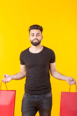 Adam sarı bir arka planda kırmızı alışveriş torbaları tutuyor. Süpermarket ve hediyeler alışveriş kavramı. Reklam alanı.