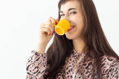 Beyaz bir arka planda ellerini poz küçük bir oyuncak sarı kupa tutan sevimli genç kadın. Favori içecekler konsepti