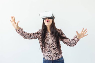 Güzel genç kadın sanal gerçeklik gözlük giyiyor ve beyaz bir arka planda ayakta iken bir oyun oynuyor. Füçizm ve yeni teknolojiler kavramı.