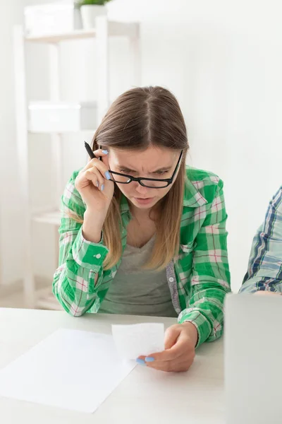 Upset young woman considers the amount of expenses for purchases and payment of credits by entering information into laptop for accounting of home bookkeeping. Concept of savings and waste.