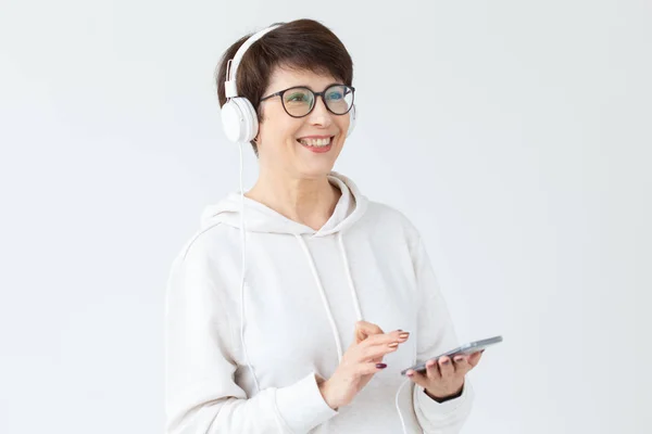 Beautiful woman 40-50 years old listening music in big headphone and holding tablet on white background — Stock Photo, Image